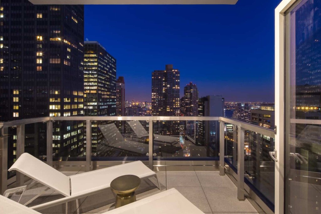 Apartment balcony with lounge chairs overlooking cityscape.