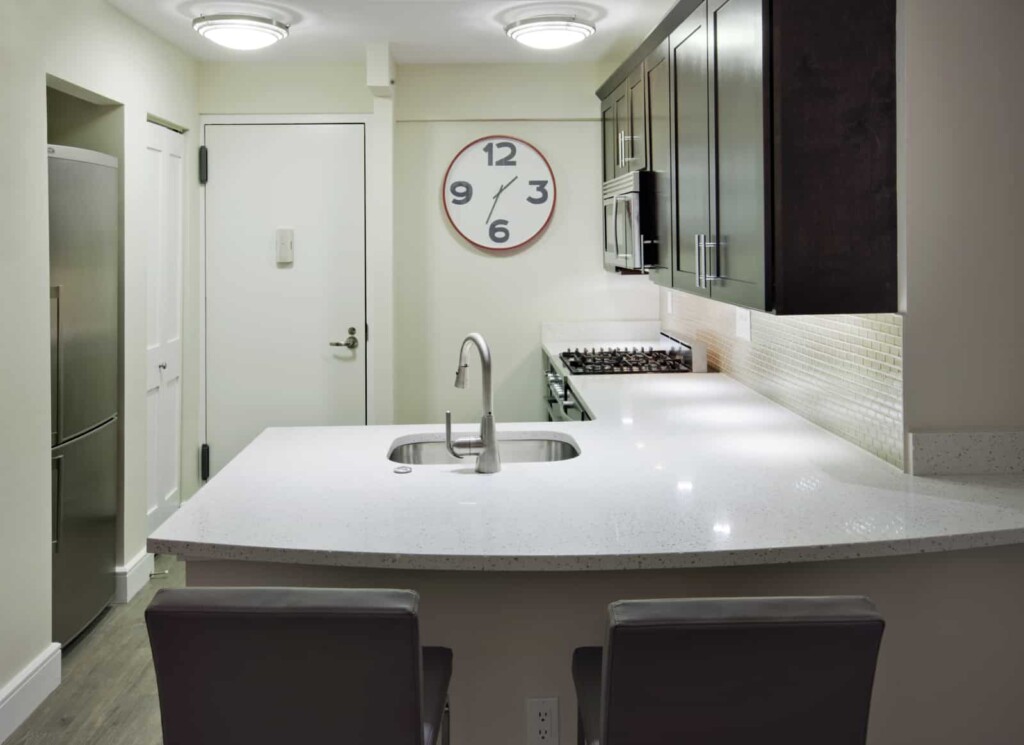 Interior of apartment kitchen with stainless steel appliances, white countertop, and seating.