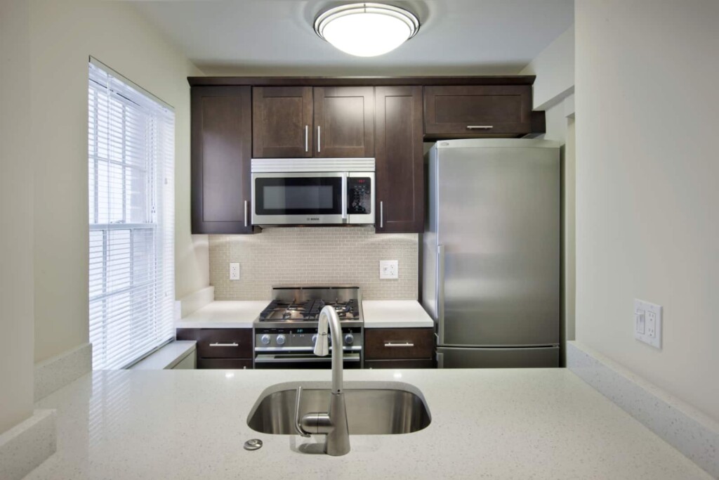 Interior of apartment kitchen with stainless steel appliances and white countertop.