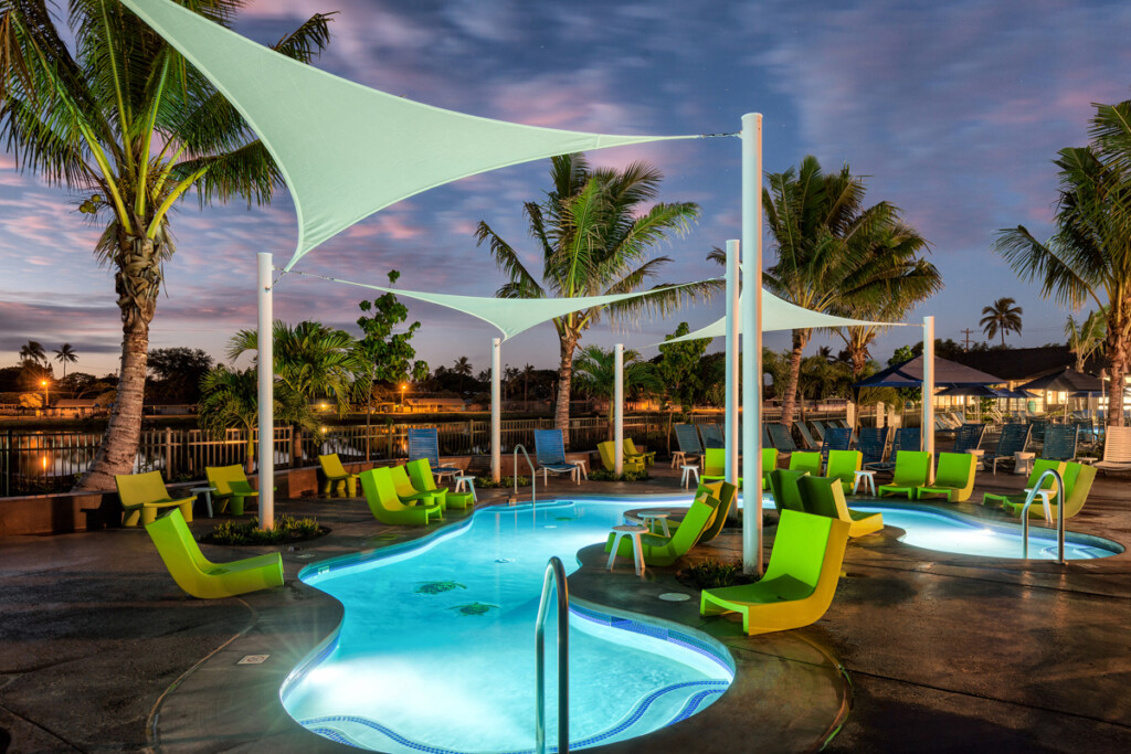 Exterior of aomebaic-shaped pool surrounded by modern deck chairs and palm trees.