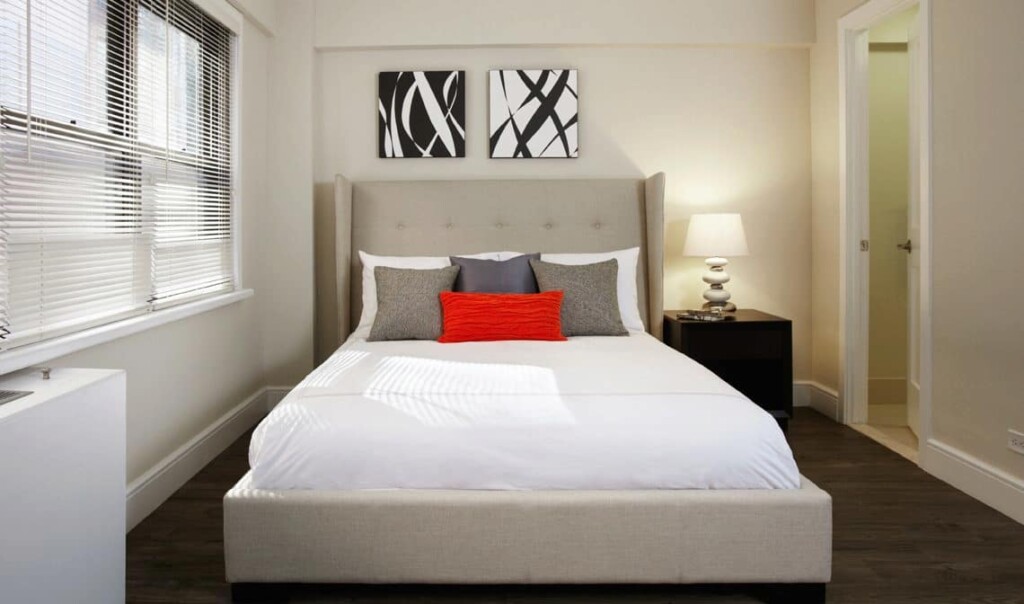 Interior of apartment bedroom with an upholstered bed, side table and lamp.