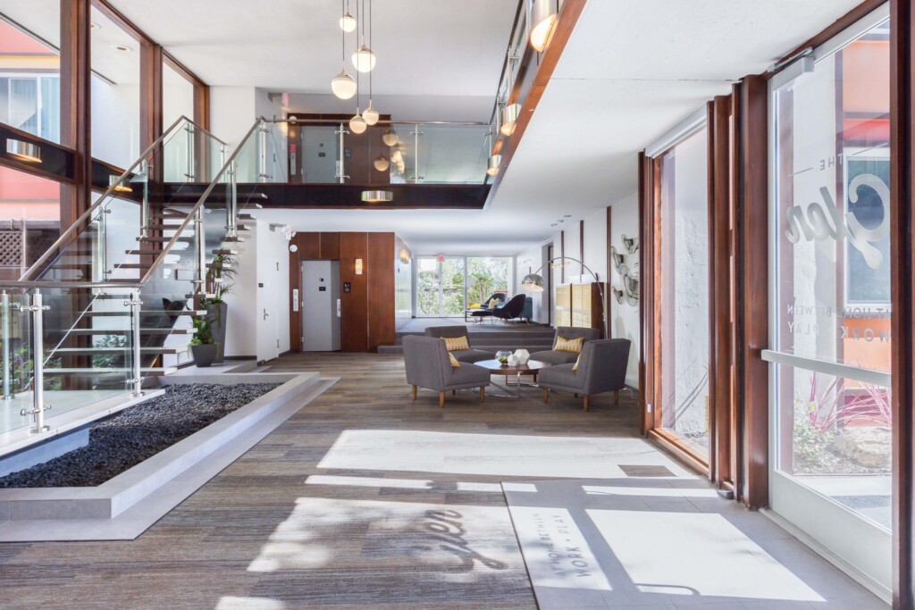 Interior of entrance to apartment complex with large floor-to-ceiling windows, glass stairway, and modern furniture