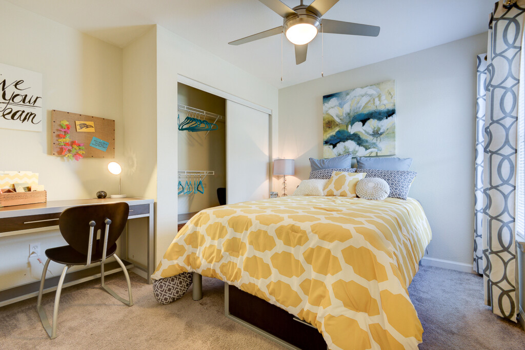 Interior of apartment bedroom with bed, closet, desk and ceiling fan