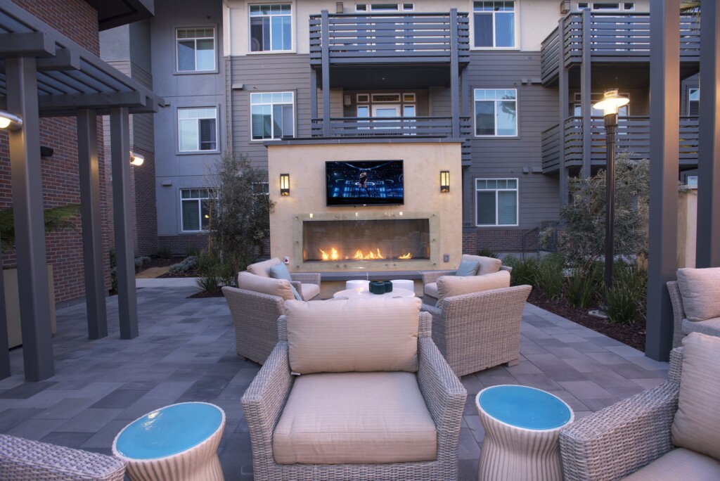 Exterior common area with seating, fireplace and large-screen television surrounded by apartment buildings