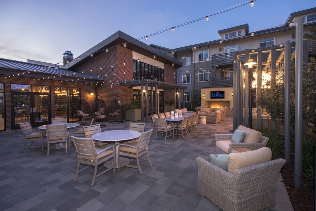 Exterior common area with dining tables, seating, fireplace and large-screen television surrounded by apartment buildings