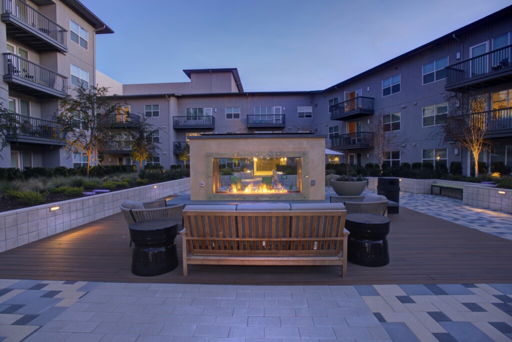 Exterior of courtyard with couches and fireplace surrounded by 3- and 4-story apartment building