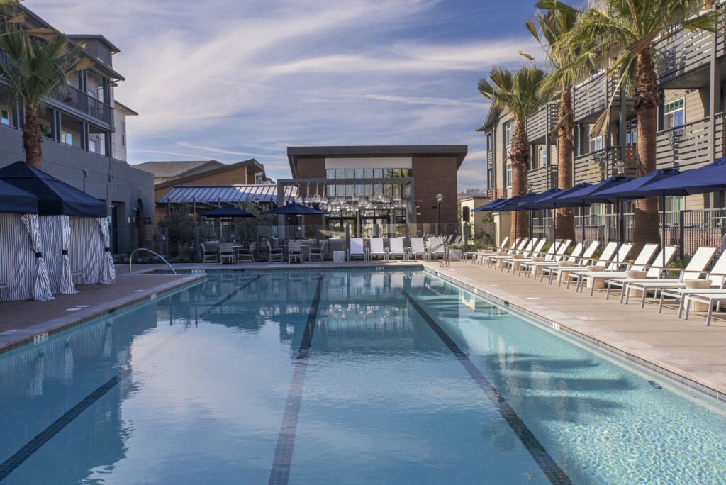 Exterior of pool with lounge chairs, umbrellas, and cabanas surrounded by apartment complex