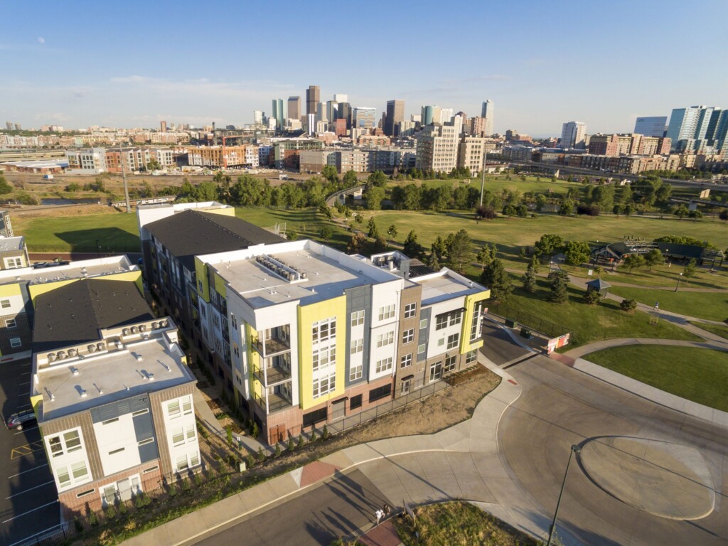 Aerial exterior of apartment complex with park and downtown skyline in background.