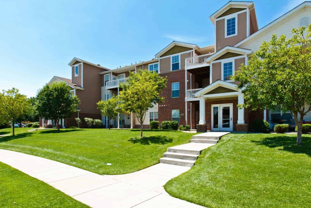 Exterior of apartment complex entrance with lawn and sidewalk in the foreground.